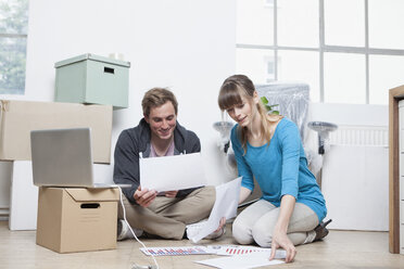 Zwei Kollegen sitzen auf dem Boden zwischen Kartons in einem Büro - RBF001717