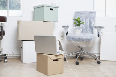 Stack of cardboard boxes, wrapped swivel chair and a notebook in an office - RBF001719