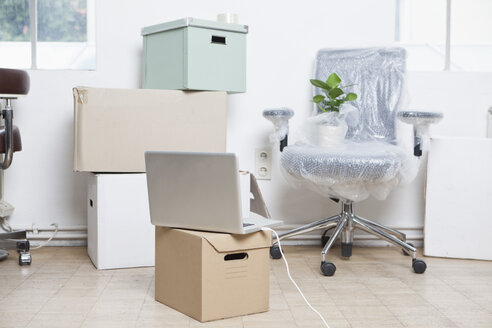 Stapel von Kartons, verpackter Drehstuhl und ein Notebook in einem Büro - RBF001719