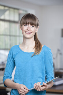 Portrait of smiling young woman with digital tablet in an office - RBF001723