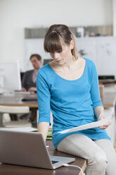 Junge Frau sitzt an ihrem Schreibtisch in einem Büro und benutzt einen Laptop - RBF001726