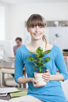 Portrait of smiling young woman with potted plant in an creative office - RBF001730