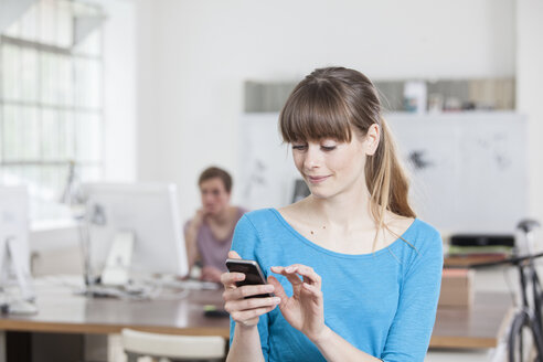 Portrait of young woman in an creative office using her smartphone - RBF001791