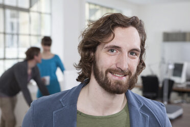 Portrait of smiling young man in a creative office - RBF001735