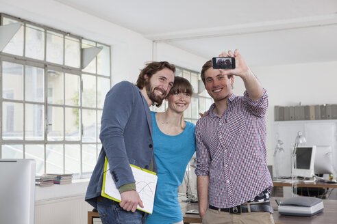 Three colleagues taking a selfie with smartphone in an office - RBF001747