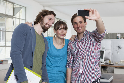 Three colleagues taking a selfie with smartphone in an office - RBF001793