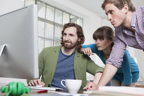 Three colleagues looking at computer in a creative office - RBF001752