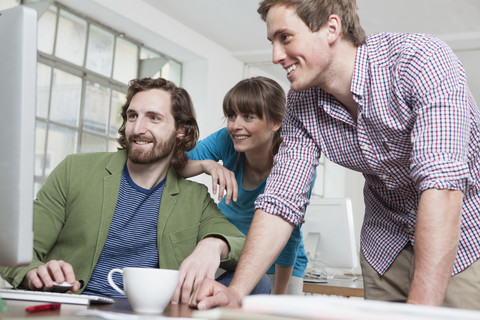 Drei Kollegen vor einem Computer in einem kreativen Büro, lizenzfreies Stockfoto