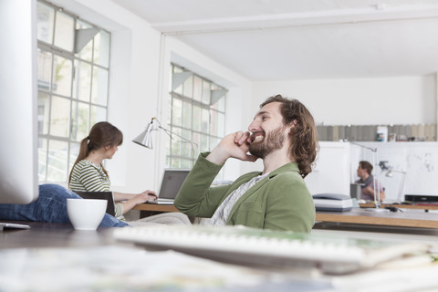 Junger Mann telefoniert an seinem Schreibtisch in einem kreativen Büro, lizenzfreies Stockfoto