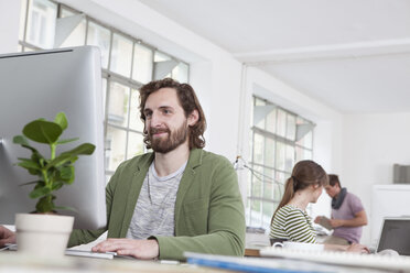 Portrait of young man working at computer in a creative office - RBF001766