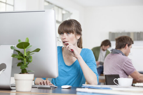 Portrait of young woman working at computer in a creative office - RBF001770