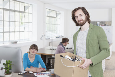 Porträt eines jungen Mannes mit einer Pappschachtel voller Stromkabel in einem kreativen Büro - RBF001771