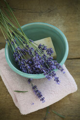 Schale mit frischen Lavendelblüten, Lavendula angustifolia, und Lavendelseife auf Handtuch und Holz - ASF005453