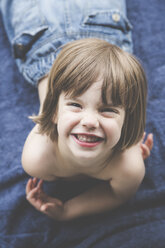 Porträt eines grinsenden kleinen Mädchens, das auf einem blauen Handtuch liegt - LVF001743