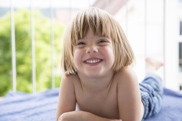 Porträt eines lachenden kleinen Mädchens, das auf einem Handtuch auf dem Balkon liegt - LVF001744