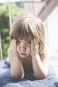 Portrait of sad little girl lying on towel on balcony - LVF001746