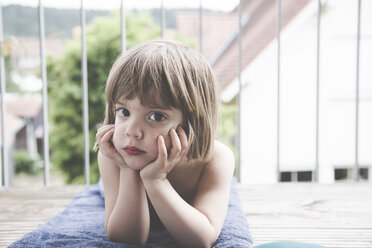 Porträt eines traurigen kleinen Mädchens, das auf einem Handtuch auf dem Balkon liegt - LVF001747