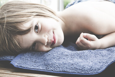 Porträt eines lächelnden kleinen Mädchens, das auf einem Handtuch auf dem Balkon liegt - LVF001753