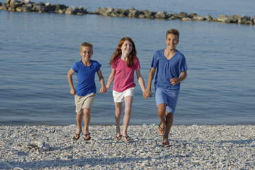 Three smiling children running hand in hand at waterside of Adria - LBF000891