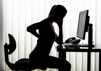 Silhouette einer Frau am Schreibtisch mit Rückenschmerzen - EJWF000456