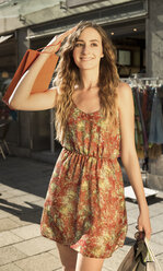 Lächelnde junge Frau mit Einkaufstüten in der Abenddämmerung - FCF000398