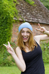 Portrait of smiling young woman with blue bonnet showing victory-sign with both hands - SEF000810
