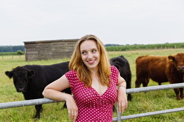 Portrait of a smiling young woman leaning on a fence cattles in the background - SEF000832