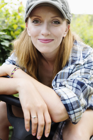 Porträt einer lächelnden jungen Frau, die auf einem Rasenmäher sitzt, lizenzfreies Stockfoto