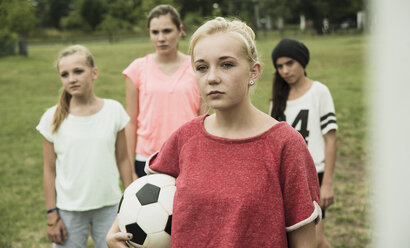 Porträt eines ernst dreinblickenden Teenagers mit Fußball vor drei anderen Mädchen - UUF001564