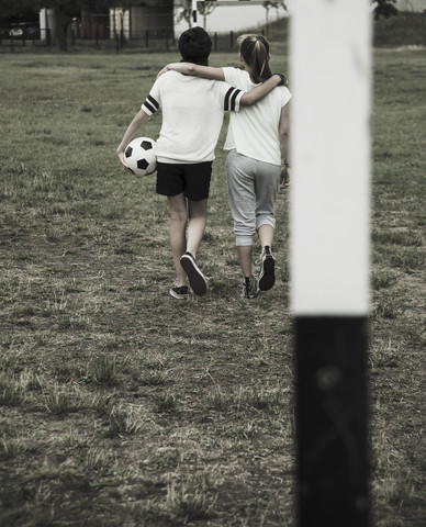 Zwei Mädchen im Teenageralter gehen auf einem Fußballplatz, Rückenansicht, lizenzfreies Stockfoto