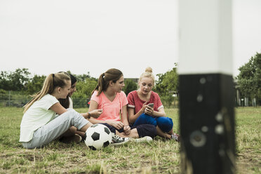 Vier Freundinnen im Teenageralter sitzen auf einem Fußballfeld und benutzen ein Smartphone - UUF001577