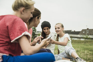 Four female teenage friends sitting on soccer field using her smartphones - UUF001579