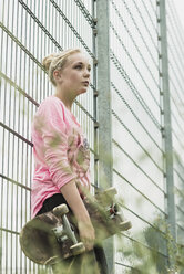 Teenager-Mädchen mit Skateboard am Zaun lehnend - UUF001581