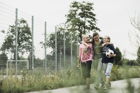Drei Teenager-Mädchen mit Fußball und Skateboard gehen nebeneinander, lizenzfreies Stockfoto