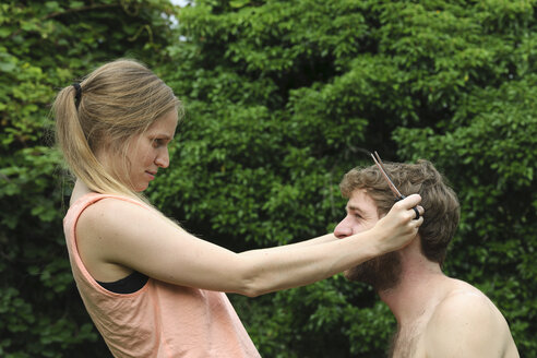 Junge Frau schneidet die Haare ihres Freundes im Garten - LAF001183