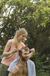 Junge Frau schneidet die Haare ihres Freundes im Garten - LAF001184