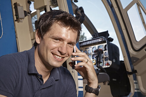 Germany, Bavaria, Landshut, Helicopter pilot using mobile phone - KDF000080