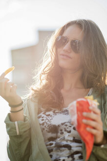 Porträt eines Teenagers mit Sonnenbrille, der eine Papiertüte mit Pommes frites hält - UUF001628