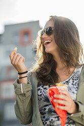 Porträt eines lachenden Teenagers mit Sonnenbrille, der eine Papiertüte mit Pommes frites hält - UUF001629