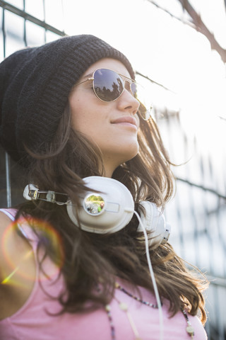 Porträt eines lächelnden Teenagers mit Kopfhörern, Sonnenbrille und Wollmütze, lizenzfreies Stockfoto