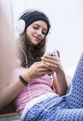 Porträt eines lächelnden Teenagers, der ein Smartphone hält und mit Kopfhörern Musik hört - UUF001599