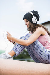 Portrait of smiling teenage girl holding smartphone hearing music with headphones - UUF001603