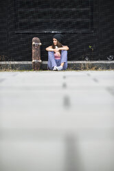 Teenager-Mädchen mit Skateboard sitzt vor einer schwarzen Fassade - UUF001609