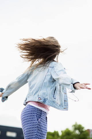 Teenage girl wearing jeans jacket jumping into the air, back view stock photo