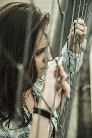 Teenage girl looking through a wire fence stock photo