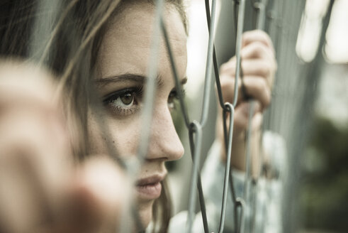 Teenage girl looking through a wire fence - UUF001642