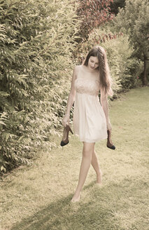 Young woman walking barefoot on meadow in the garden - FCF000406