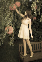 Portrait of young woman standing on a garden bench at twilight - FCF000407