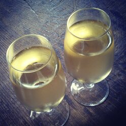 Two glasses of white wine on a wooden table - HAWF000429