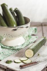 Colander of courgettes and a knife and slices of courgettes on chopping board - SBDF001215